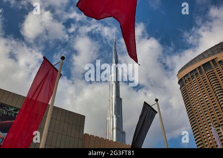 Looking up at the world's tallest building, the Burj Khalifa in Dubai, the UAE, showing the top two thirds with flags and buildings at ground level Stock Photo
