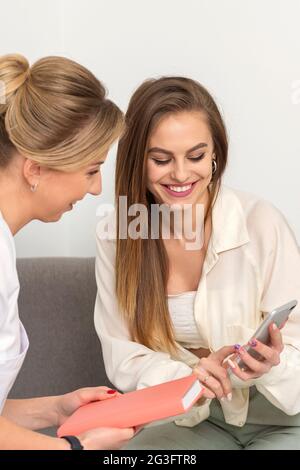 Two young women doctor with patient smiling and looking at smartphone sitting in hospital office, consultation with a doctor Stock Photo