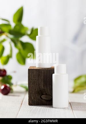 White tubes with cosmetics on a wooden podium against the background of foliage, cherry berries. Natural cosmetics.  Stock Photo