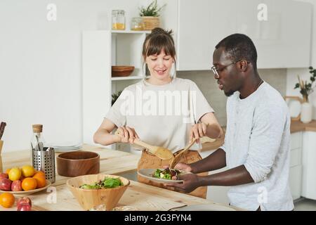 Young couple preparing vegetable salad together in the kitchen Stock Photo