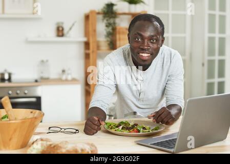 Portrait of African young man smiling at camera while working onlaptop during lunch Stock Photo