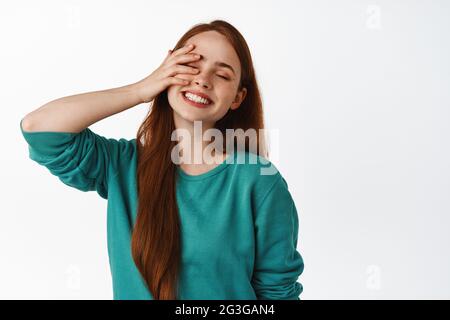 Carefree redhead woman laughing, smiling white teeth, close eyes and touch face gently, feeling free and happy, standing over white background Stock Photo