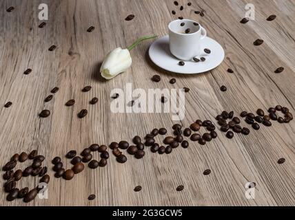 Coffee beans form the word "buongiorno" (good morning in Italian) with a cup of espresso on which other beans fall Stock Photo