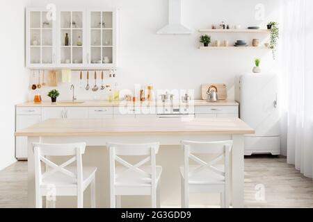 Style minimalism. Stylish kitchen in white and brown wood. Dining table, utensils and kitchenware on shelves Stock Photo