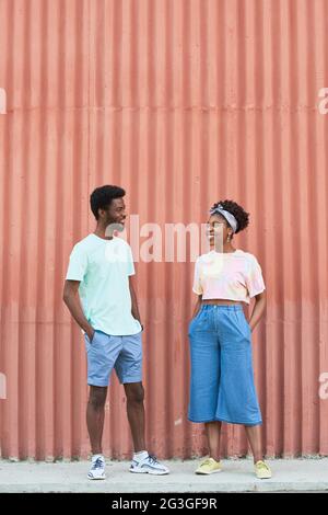 Young people talking and laughing while standing outdoors against the red wall Stock Photo