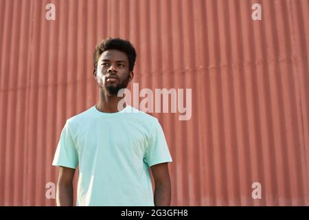 African young man looking away while standing in the city against the red wall Stock Photo