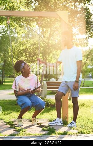 Happy African couple riding on a swing and talking in the park Stock Photo