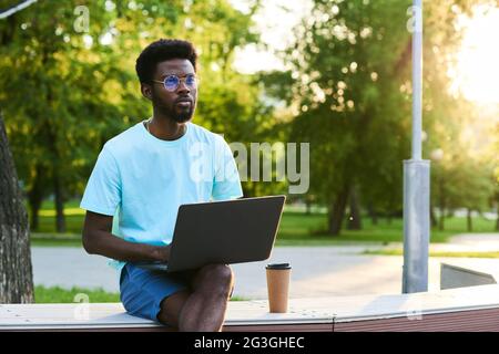 Serious African businessman working online on laptop while sitting in the park outdoors Stock Photo