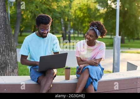 African happy couple using laptop and working online together while sitting in the park Stock Photo