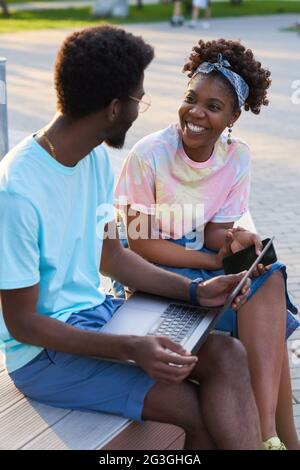 Happy African couple talking to each other and working on laptop outdoors Stock Photo