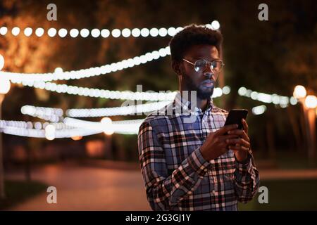 African young man using mobile phone while standing in the park in the evening Stock Photo