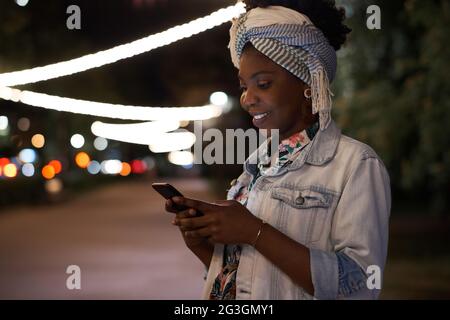 African woman reading a message on the phone while standing in the city in the evening Stock Photo