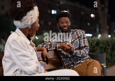 African young couple sitting on the bench and talking during their date in the park Stock Photo
