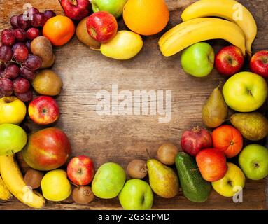 Frame from multi-colored different fruits on a wooden background. Harvest fruits top view. Bananas, apples and pears. Lemon, mango, avocado and grapes Stock Photo