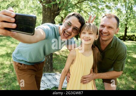 Gay male couple making selfie portrait on mobile phone with daughter in the park Stock Photo