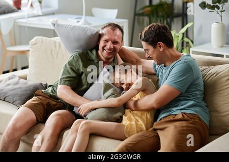Happy family of three playing together while sitting on sofa in the living room Stock Photo