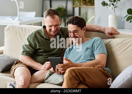 Two friends using tablet pc together while sitting on sofa in the room at home Stock Photo