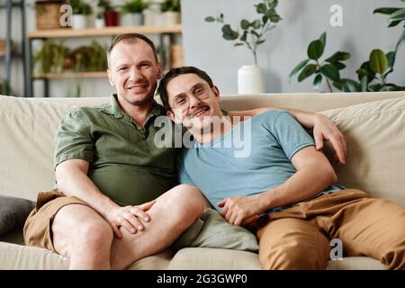 Portrait of happy male gay couple smiling at camera while sitting on sofa in the room Stock Photo