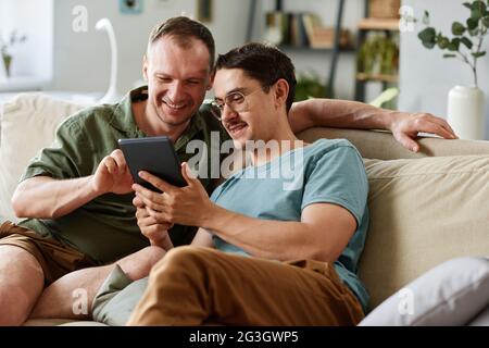 Two friends watching something on digital tablet while sitting on sofa in the room Stock Photo