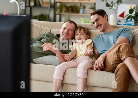 Gay family with their adopted daughter watching TV together on the sofa at home Stock Photo