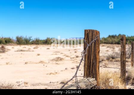 Wooden fence post with rusty barbed wire in a sandy field Stock Photo