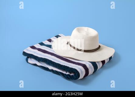 Large woman’s white brim hat on a striped beach towel with a light blue background Stock Photo