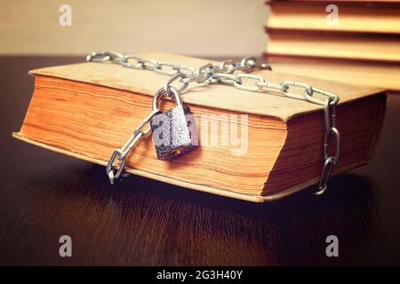 old book wrapped with chain and locked on padlock on table, concept, toned Stock Photo