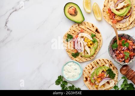 Mexican tacos with grilled chicken, avocado, corn kernels, tomato, onion, cilantro and salsa at white stone table. Traditional Mexican and Latin ameri Stock Photo