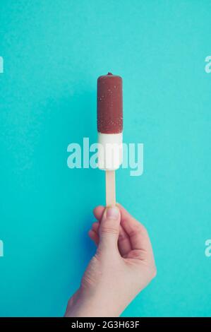 vanilla ice cream with chocolate on a stick held by a child's hand, with copy space against mint green background Stock Photo