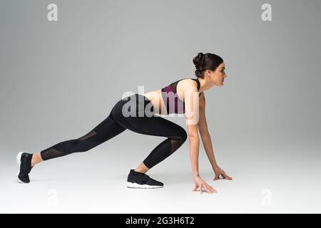 side view of woman wearing black sportswear in low start position on grey background Stock Photo