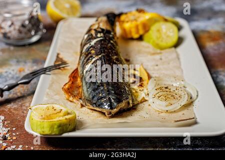 Close-up delicious roasted mackerel with vegetables on a rectangular plate. Appetizing grilled sea fish with corn, zucchini and spiced lemon. Mediterr Stock Photo