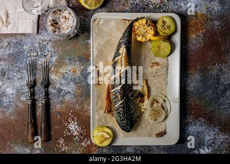 Delicious grilled mackerel with vegetables on a rectangular plate. Appetizing roasted sea fish with corn, zucchini and spiced lemon. Mediterranean Kit Stock Photo