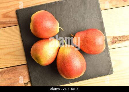 Several organic yellow-red pears on a slate board, on a wooden table, top view. Stock Photo
