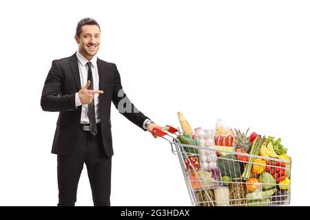 Businessman standing with a shopping cart full of food and pointing isolated on white background Stock Photo