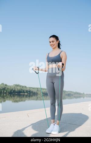 Smiling young woman exercising with resistance band on a riverside Stock Photo