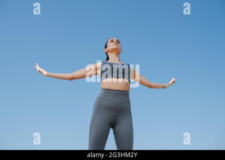 Majestic young woman in sportswear greetng the sun. Over blue sky Stock Photo
