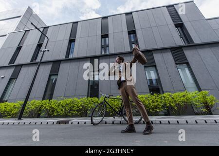 full length of joyful businessman in formal wear talking on cellphone near building Stock Photo