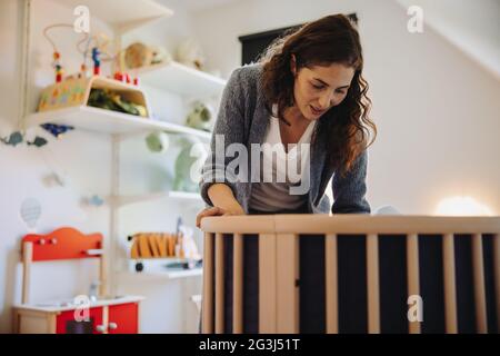 Woman putting her baby to sleep in crib. Caring mother standing at the crib and looking at her baby. Stock Photo