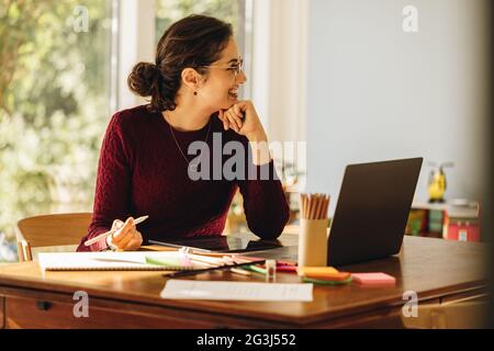 Female artist working from home. Illustrator sitting at home looking away and smiling. Stock Photo