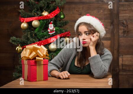 Beautiful girl sitting at the table with a present near New Year tree Stock Photo