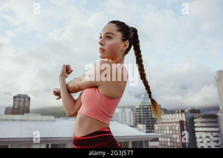 Young woman exercising outdoors on rooftop. Sportswoman stretching her arm outdoors. Stock Photo