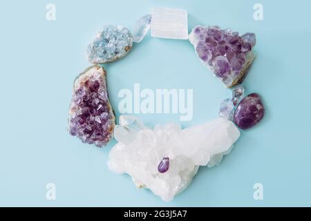 Round frame made out of and raw natural crystal geode clusters, amethyst, celestite, quartz on light blue background for copy space. Stock Photo