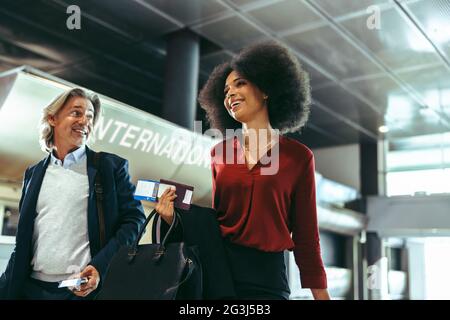 Business travelers walking together and talking at airport. Business people walking through airport terminal to catch their flight. Stock Photo