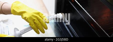 Female hands in yellow gloves are holding a steam cleaner and cleaning oven Stock Photo