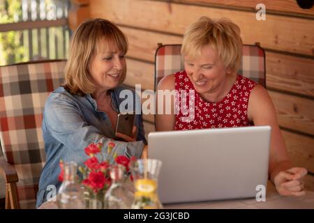 Senior women laugh together using and looking at laptop at home. Stock Photo