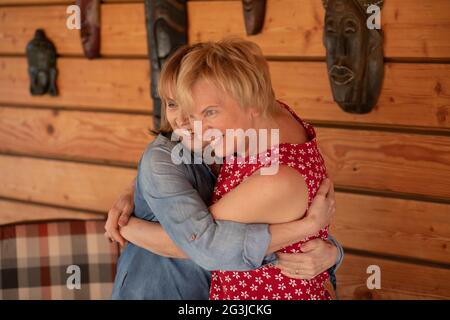 Two women 55 years old girlfriends hugging on the background of wooden wall Stock Photo