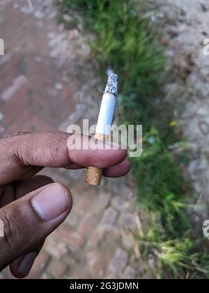 Selective focus of cigarette between fingers of a person's hand against a  blurred background Stock Photo