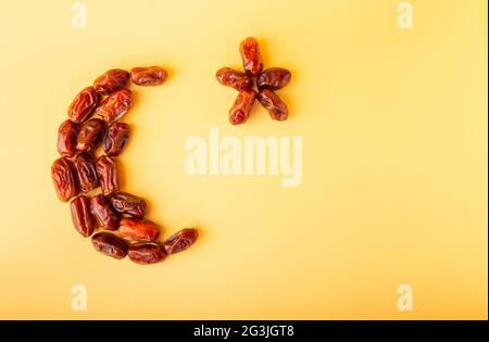Ramadan kareem with dried dates arranged in shape of crescent moon on yellow background. Iftar food concept. Space for text. Stock Photo