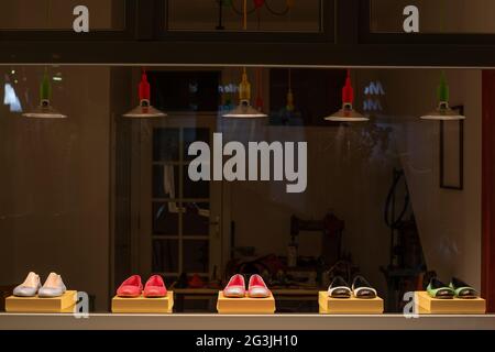 Shoes in a window display of a shoemaker workshop at night. A cobbler sewing machine is visible in the background. Stock Photo