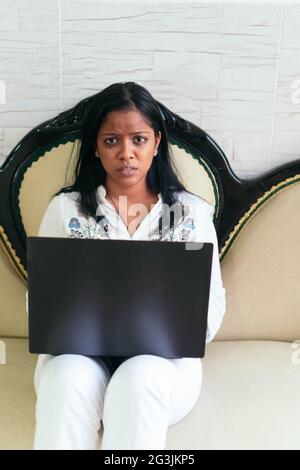 A sad African girl works at home, sits on the couch and looks into the camera. Stock Photo